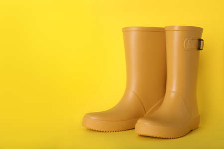 Pair of bright rubber boots on yellow background. Space for text