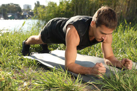 Sporty man doing plank exercise on green grass near riverの写真素材