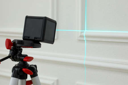 Cross line laser level on tripod in front of white wall
