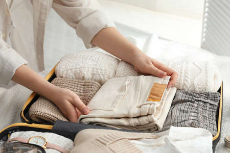 Woman packing suitcase for trip on bed, closeup