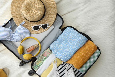 Open suitcase full of clothes and summer accessories on bed, flat layの写真素材