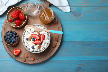 Bowl of fresh cottage cheese, berries with almond and ingredients on light blue wooden table, flat lay. Space for textの写真素材