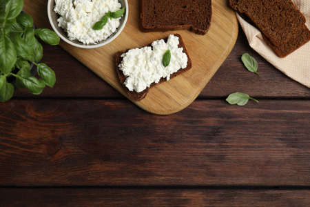 Bread with cottage cheese and basil on wooden table, flat lay. Space for textの写真素材