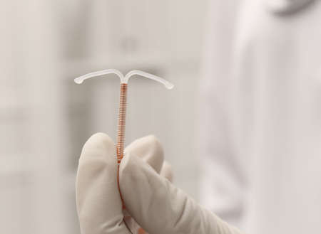 Doctor holding T-shaped intrauterine birth control device on blurred background, closeupの写真素材
