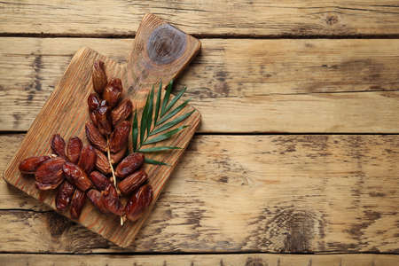 Sweet dried dates with green leaf on wooden table, top view. Space for text