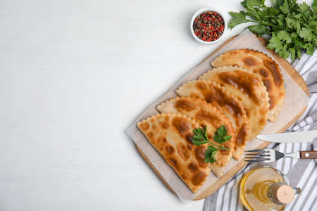 Delicious fried chebureki and ingredients served on white table, flat lay. Space for textの写真素材