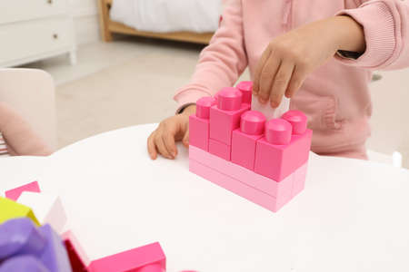Cute little girl playing with colorful building blocks at table indoors, closeup. Space for textの写真素材