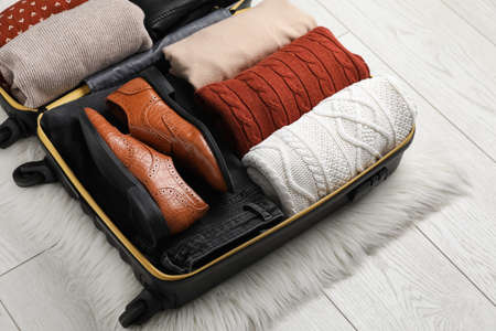 Open suitcase with folded clothes, shoes and accessories on floorの写真素材