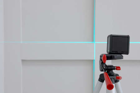 Cross line laser level on tripod in front of light wallの写真素材