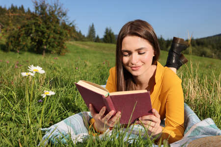 Beautiful young woman reading book on green meadowの写真素材