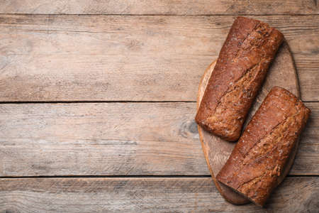 Cut rye baguette on wooden table, top view. Space for text