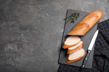 Cut tasty baguette with knife on gray table, flat lay. Space for text