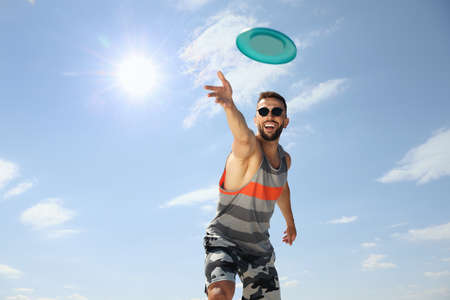 Happy man throwing flying disk against blue sky on sunny dayの写真素材