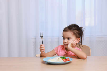 Cute little girl refusing to eat her breakfast at home, space for textの写真素材