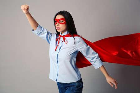 Confident young woman wearing superhero cape and mask on light gray backgroundの写真素材