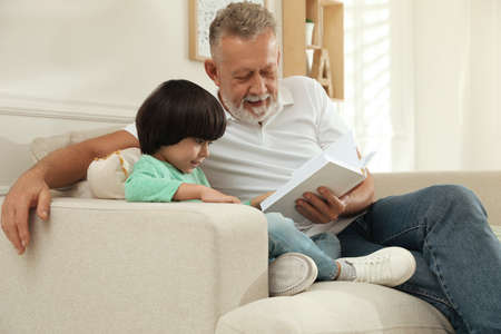 Happy grandfather with his grandson reading book together at homeの写真素材
