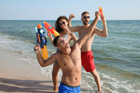 Friends with water guns having fun on beachの写真素材
