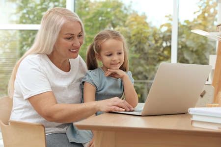 Happy grandmother and her granddaughter using laptop together at homeの写真素材