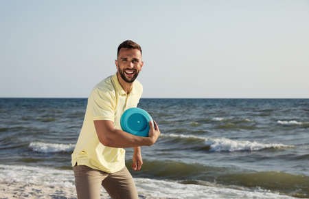 Happy man throwing flying disk at beach on sunny dayの写真素材