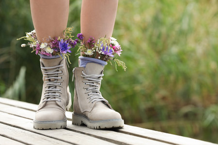 Woman standing on wooden pier with flowers in socks outdoors, closeup. Space for textの写真素材