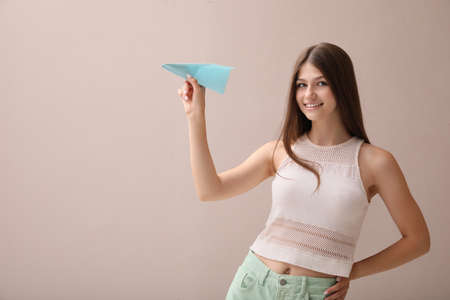 Beautiful teenage girl with paper plane on beige background. Space for textの写真素材