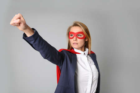Confident businesswoman wearing superhero cape and mask on light gray backgroundの写真素材