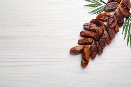 Branch of sweet dried dates with green leaves on white wooden table, flat lay. Space for textの写真素材
