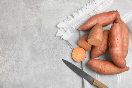 Whole and cut ripe sweet potatoes on gray table, top view. Space for text