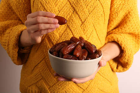 Woman with bowl of tasty sweet dried dates on light background, closeup