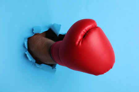 Man breaking through light blue paper with boxing glove, closeupの写真素材
