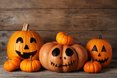 Orange pumpkins and three with drawn spooky faces on wooden table. Halloween celebration