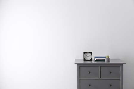 Books, houseplant and clock on chest of drawers near white wall indoors, space for text. Interior designの写真素材