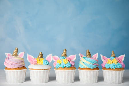 Many cute sweet unicorn cupcakes on white wooden table against light blue backgroundの写真素材