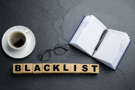 Wooden cubes with word Blacklist, cup of coffee and office stationery on slate table, flat layの写真素材