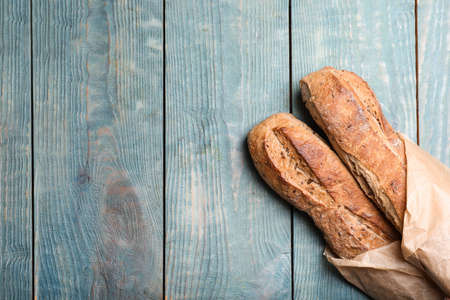 Tasty buckwheat baguettes in package on light blue wooden table, top view. Space for text
