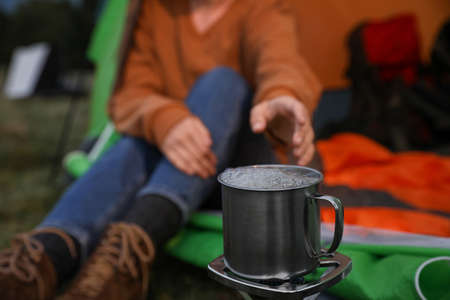Woman taking cup off stove while sitting in camping tent outdoors, closeupの写真素材
