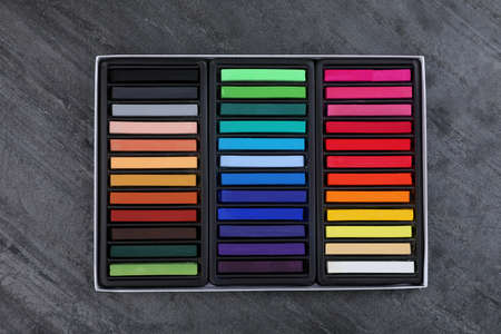Set of colorful pastels in box on gray stone table, top view. Drawing materials