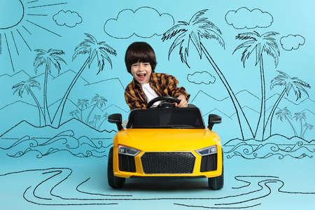 Cute little boy driving toy car and drawing of tropical resort on light blue background