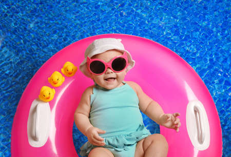 Cute little baby with inflatable ring in swimming pool, top view