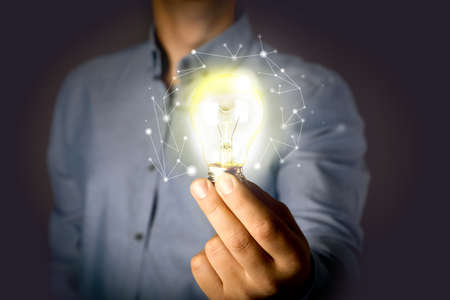 Glow up your ideas. Man holding light bulb on dark background, closeup