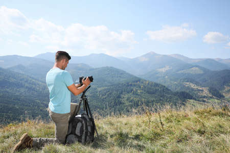 Professional photographer taking picture with modern camera in mountains. Space for text