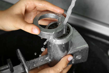 Woman washing manual meat grinder under tap water in kitchen sink indoors, closeup