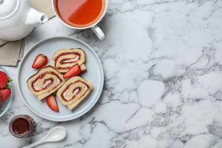 Tasty cake roll with strawberry jam and cream on white marble table, flat lay. Space for textの写真素材