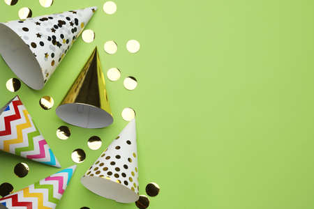 Bright party hats and shiny confetti on light green background, flat lay. Space for text