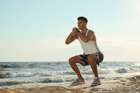 Sporty man doing exercise on sandy beach at sunsetの写真素材