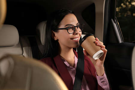 Young woman with cup of drink in modern taxi