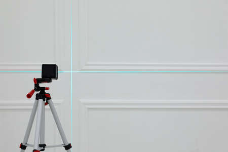 Cross line laser level on tripod in front of white wall