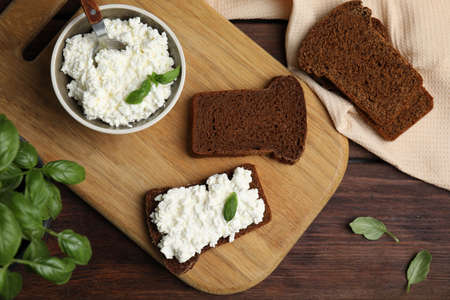 Bread with cottage cheese and basil on wooden table, flat lay