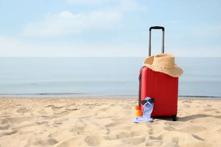 Red suitcase with beach items on sandy seashore, space for textの写真素材