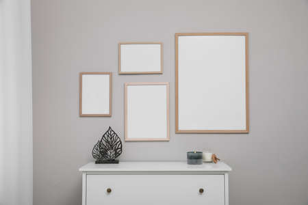 Empty frames hanging on gray wall over white chest of drawers. Mockup for design